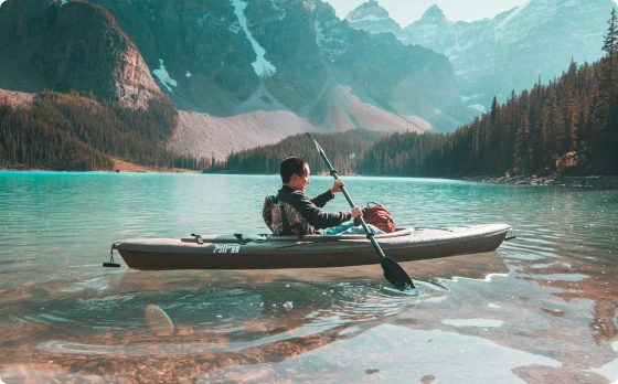 Person kayaking on a serene lake with mountains in the background