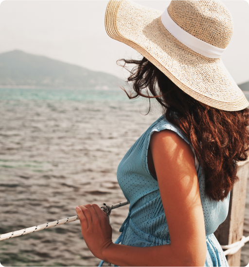 Woman in a blue dress and straw hat looking at the ocean