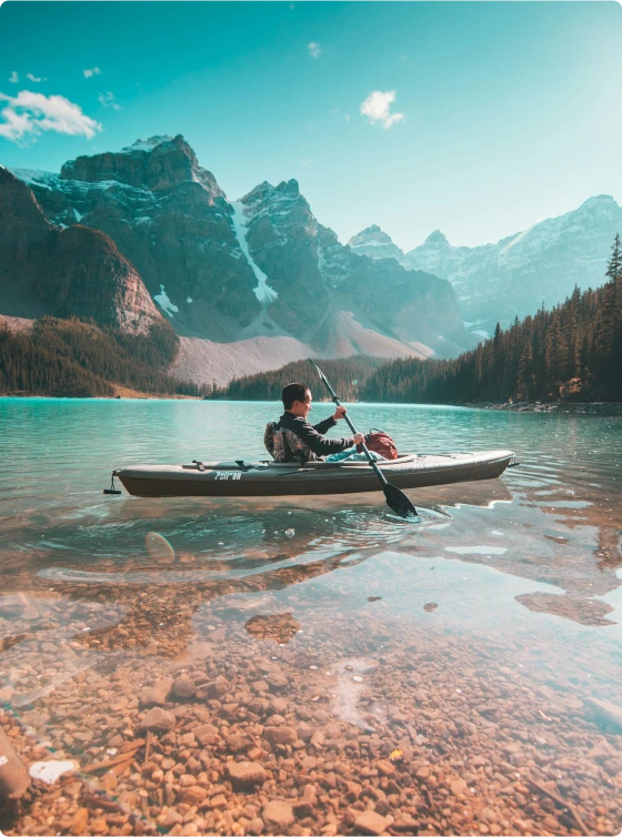 Person kayaking on a serene lake with mountains in the background